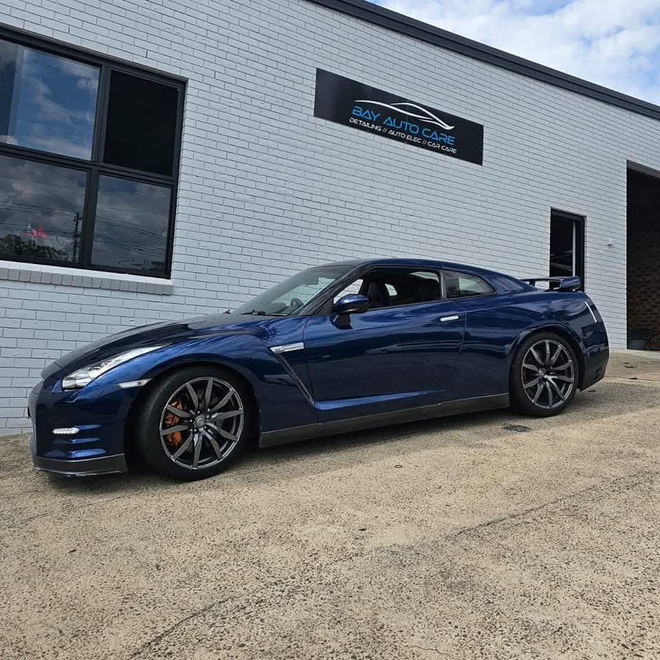 A dark blue Nissan GT-R parked outside the Bay Auto Care workshop beneath the sign