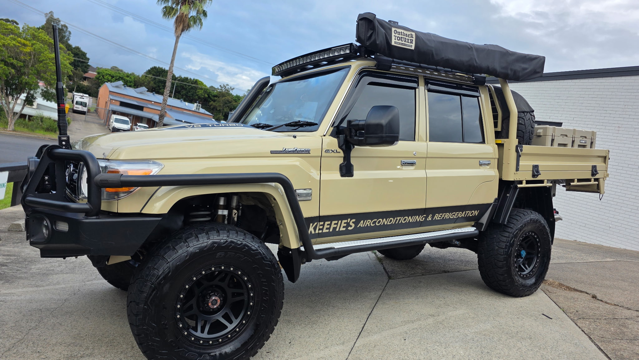 A beige Toyota LandCruiser tray ute with rooftop tent, signwritten for a refrigeration business, after detailing